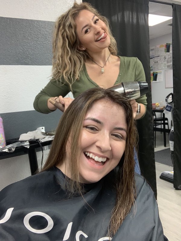 Stylist blow-drying a smiling client's hair inside the salon